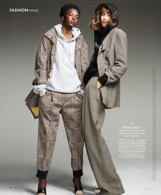 Two fashion models pose indoors wearing plaid jackets and pants in a studio setting, with one model in a hoodie.