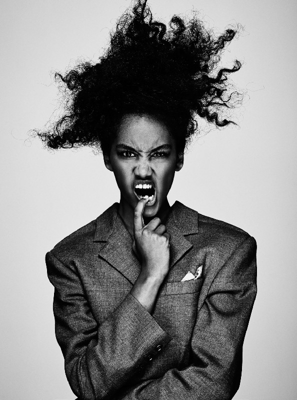 Striking black and white portrait of an adult female with voluminous afro-textured hair, wearing an oversized blazer, making an intense expression.