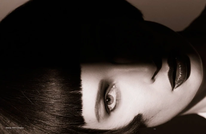 Close-up portrait of a woman with dark blunt-cut bangs, glossy dark lips, and dramatic low-key lighting styling by Katsumi Matsuo.