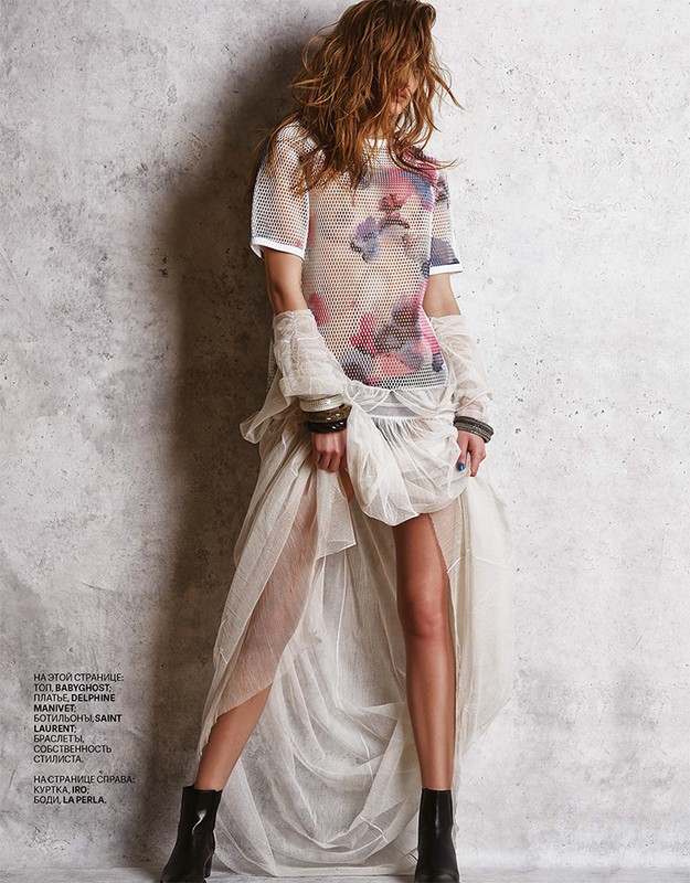 Model in mesh floral top and layered sheer white skirt with black boots standing against textured grey wall