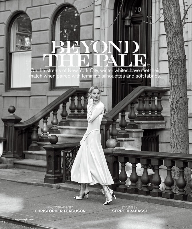 A woman in a white dress walks in front of a brownstone building, captured in a black and white fashion editorial on a city street.