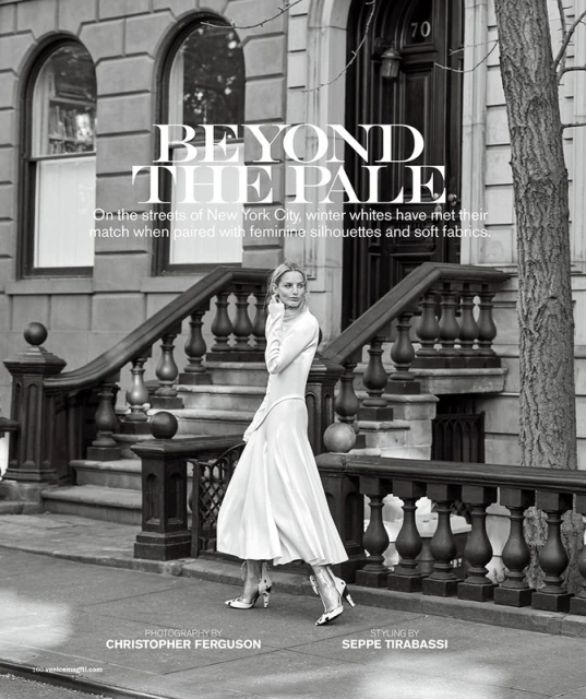 A woman in a white dress walks in front of a brownstone building, captured in a black and white fashion editorial on a city street.