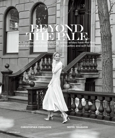 A woman in a white dress walks in front of a brownstone building, captured in a black and white fashion editorial on a city street.