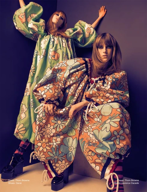 Two fashion models pose in a photo studio. They are wearing floral-print oversized dresses and platform shoes in a close-up shot.