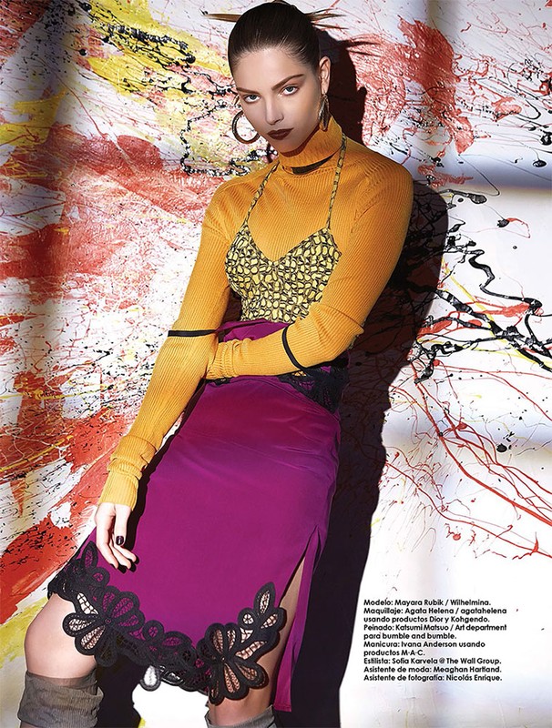 Portrait of a female fashion model wearing an orange turtleneck, patterned top, purple skirt with black trim, and gray boots.