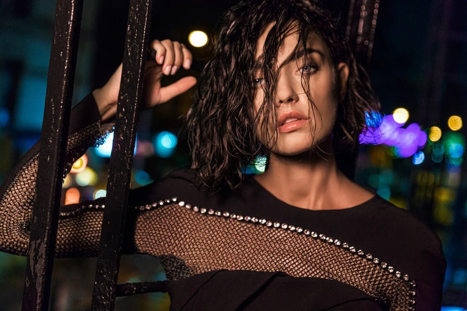 Woman with wet hair and black dress poses against a city backdrop at night, portrait shot emphasizing fashion and beauty.