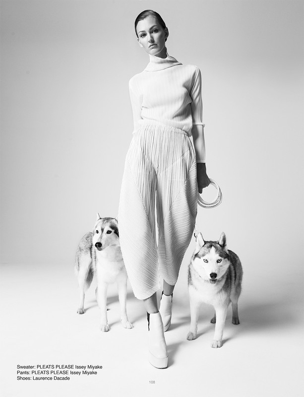 Fashion shot of a woman in white outfit with two huskies in a studio setting, highlighting minimalist style and canine companionship.