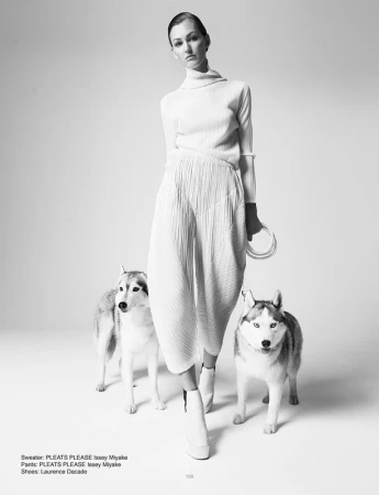 Fashion shot of a woman in white outfit with two huskies in a studio setting, highlighting minimalist style and canine companionship.