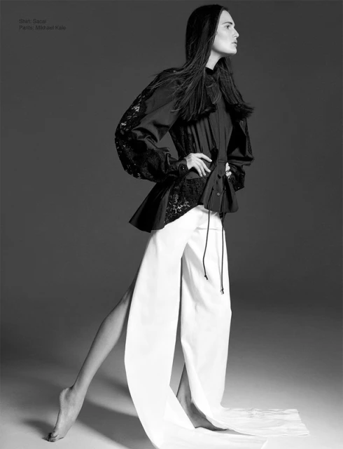 Fashion model in black top with lace sleeves and white palazzo pants strikes a pose against a neutral background in a studio shot.