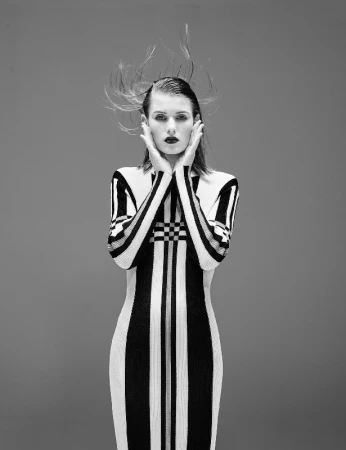 Model wearing a black and white striped dress with hands on face against a grey backdrop
