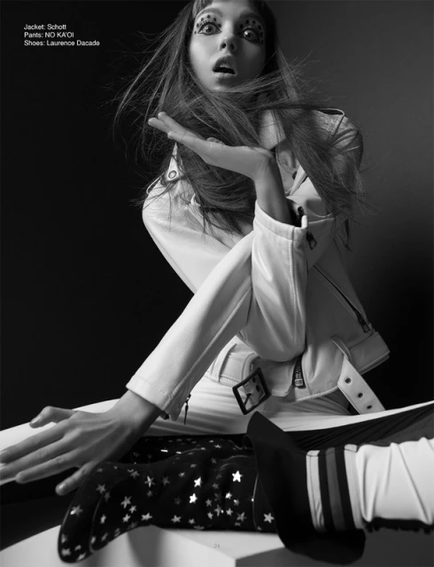 Fashion editorial shot: A young woman with dramatic eye makeup and a white jacket strikes a pose against a dark studio backdrop.