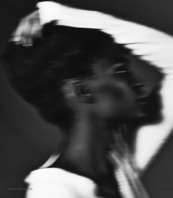 Artistic black and white portrait of a person with dark hair and a white shirt, capturing motion blur and a sense of dynamic movement.