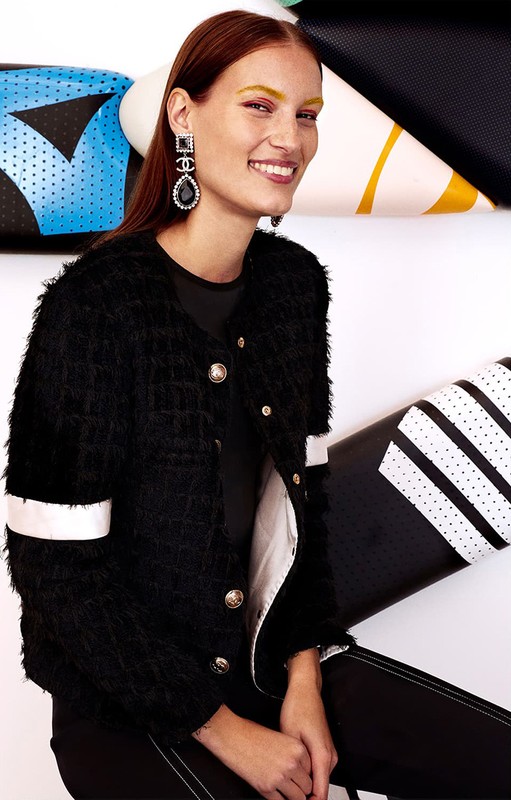 Elegant adult woman smiles in a black jacket and crystal earrings, posing in front of a patterned white, blue, and black surface.