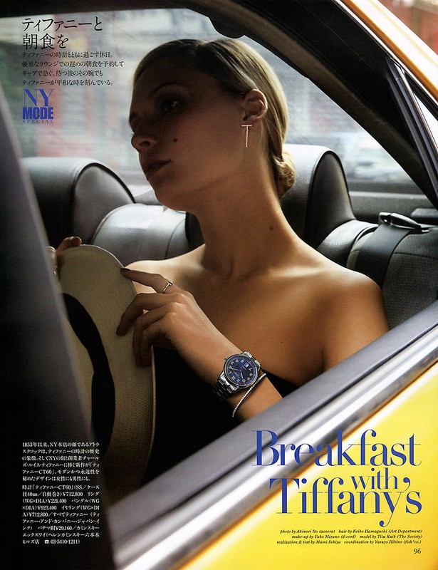 Blonde woman in a yellow taxi, wearing jewelry and a watch, holds a hat in a fashion editorial shot, referencing Breakfast at Tiffany's.