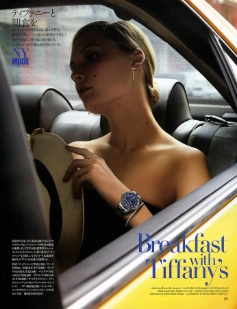 Blonde woman in a yellow taxi, wearing jewelry and a watch, holds a hat in a fashion editorial shot, referencing Breakfast at Tiffany's.
