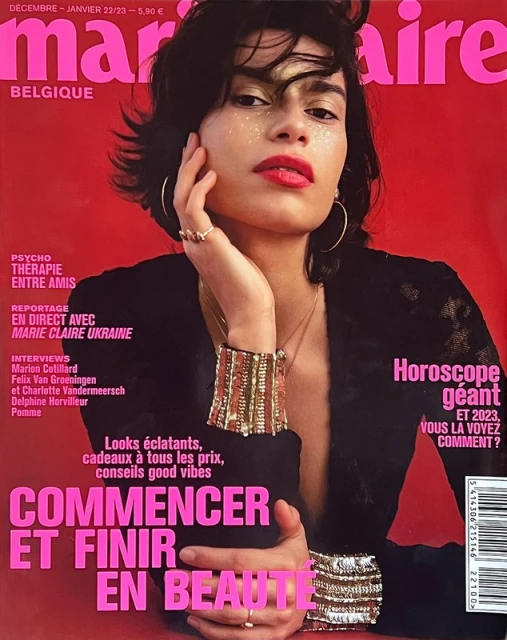 Magazine cover featuring a portrait of a woman with short dark hair, red lipstick, gold jewelry, and glitter around her eyes.