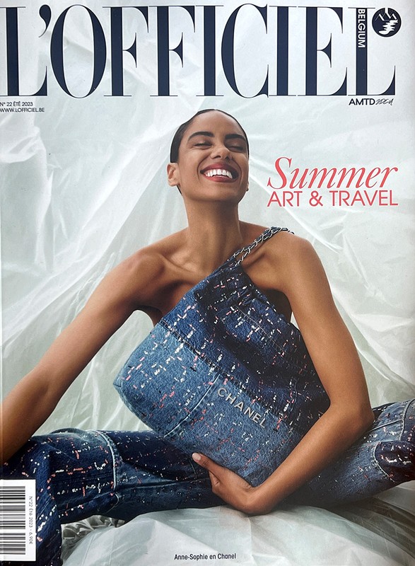 L'Officiel Belgium cover featuring a smiling woman holding a Chanel handbag, wearing matching denim pants, in a photo studio setting.