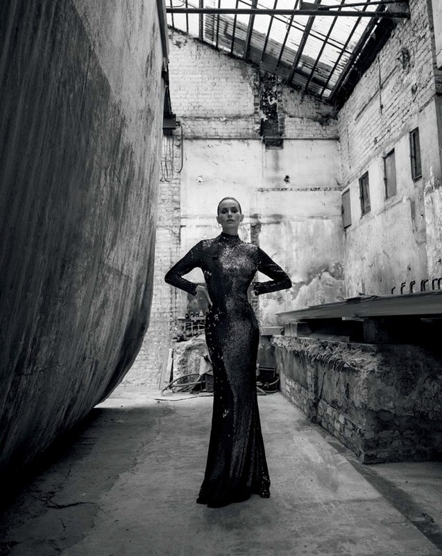Woman in a long shimmering black dress stands in an industrial-style abandoned building, posing with her hands on her hips.