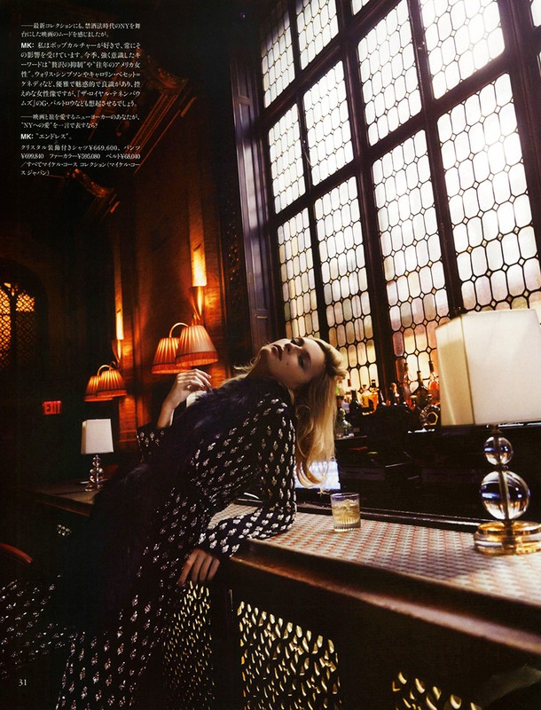 Woman in patterned outfit leans against a bar counter with a drink. Soft light streams through the window in a dimly lit interior.