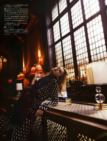 Woman in patterned outfit leans against a bar counter with a drink. Soft light streams through the window in a dimly lit interior.