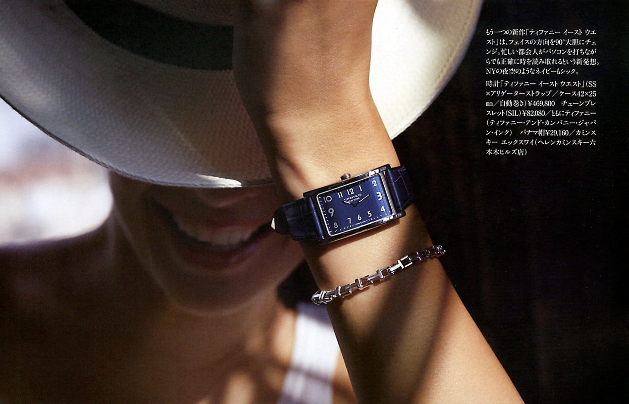 Close-up of a woman wearing a rectangular wristwatch on a blue leather band, complemented by a link bracelet and a panama hat.