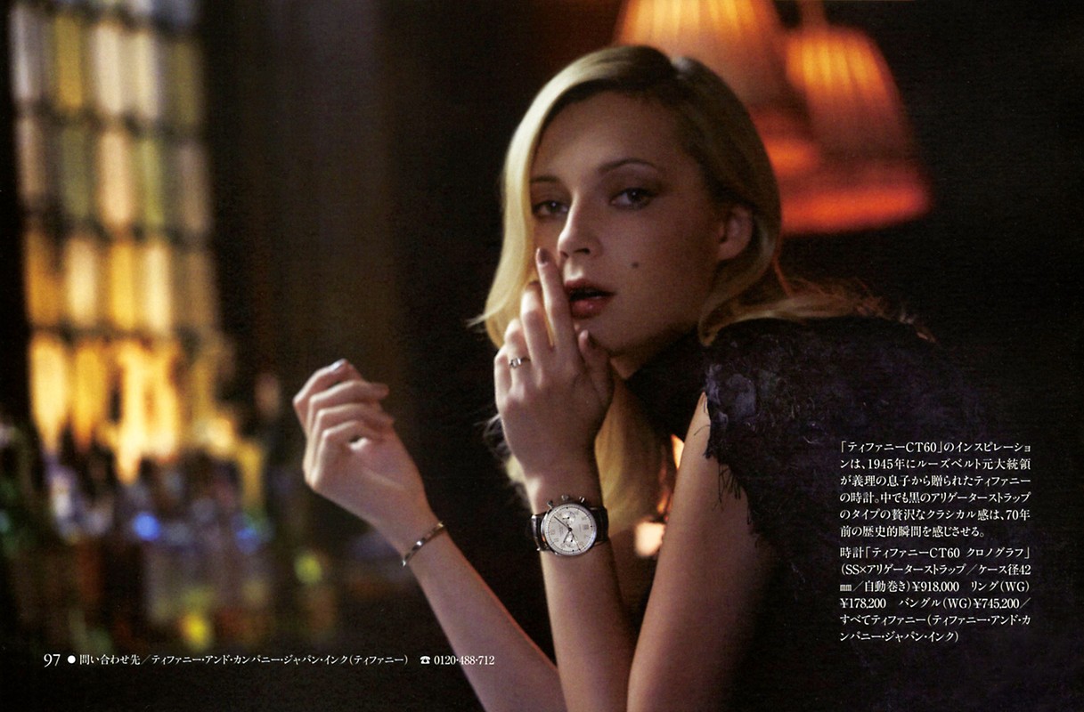 Glamorous blonde woman in dim light showcases watch, bracelet, and ring jewelry. Fashion shot with selective focus and elegant presentation.
