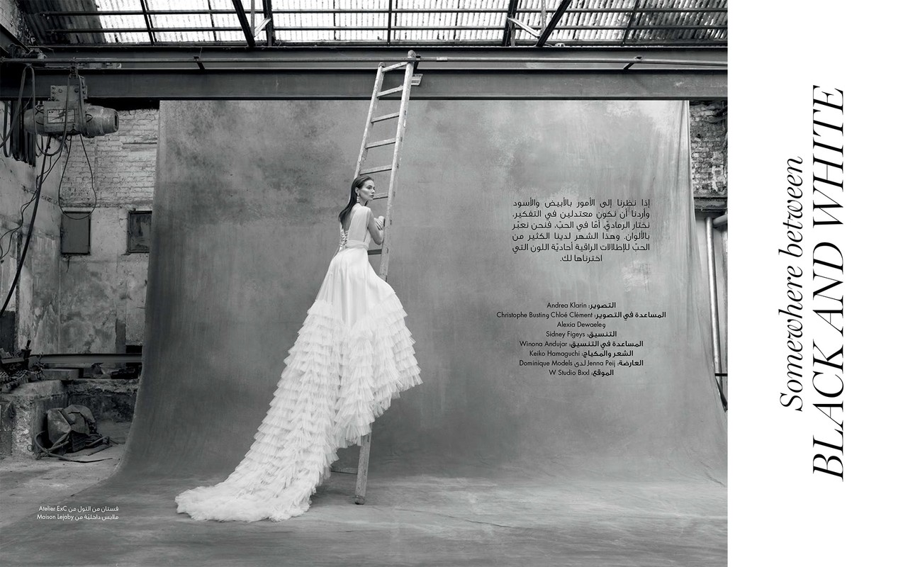 Model in white ruffled gown standing on a tall wooden ladder in an industrial studio with a textured backdrop