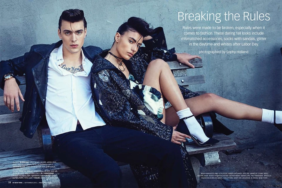 Editorial fashion shot of a young adult couple in a retro style, wearing trendy outfits, seated on a park bench in an urban outdoor setting.