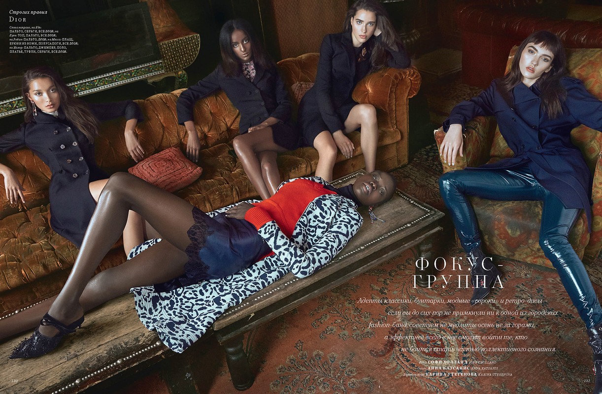 Fashion editorial shot featuring five female models in stylish clothing, posing on a couch and ottoman in an indoor setting with patterned textiles.
