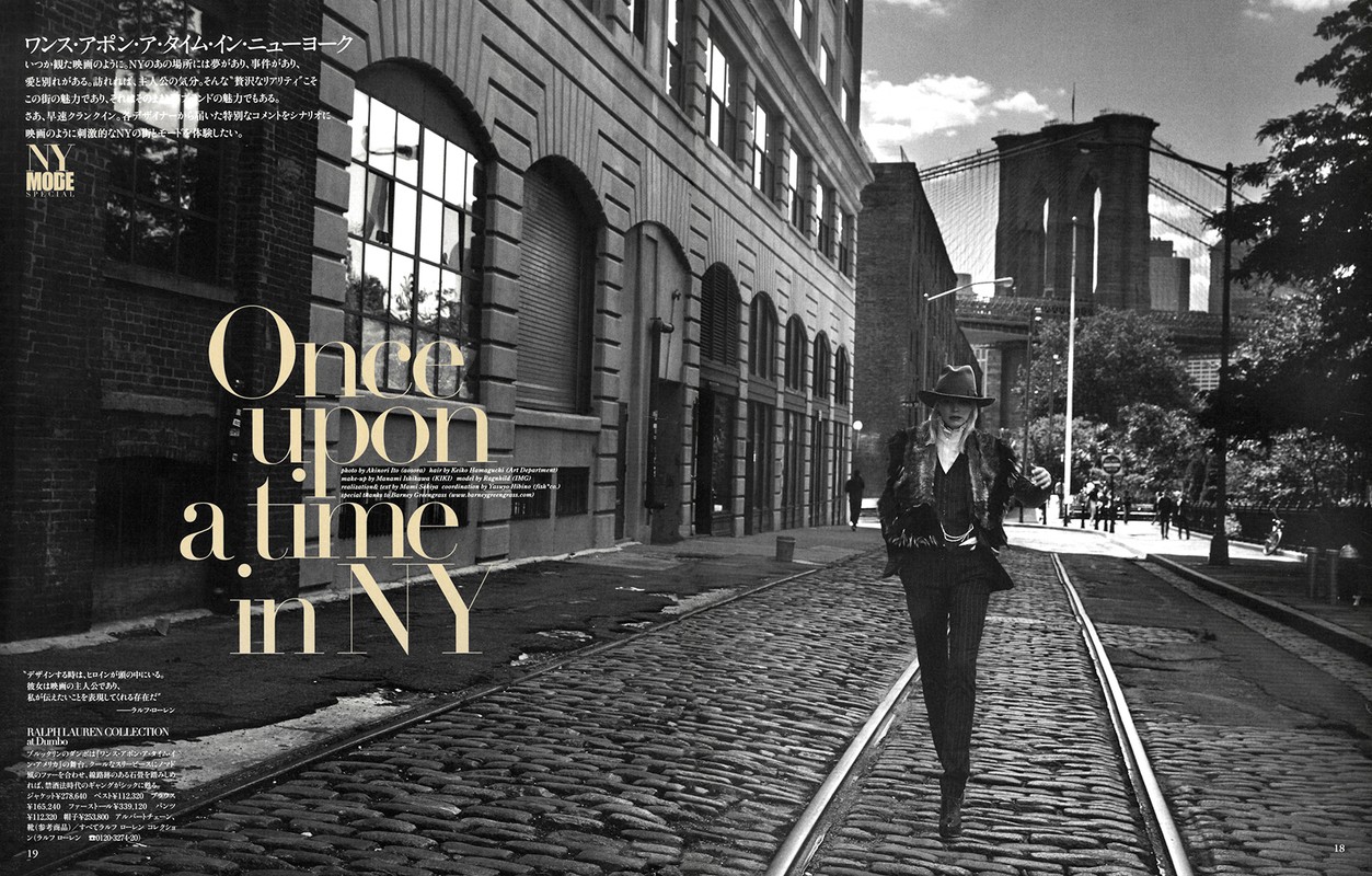 Black and white fashion editorial photo in New York City features a model wearing a dark suit on a cobblestone street near Brooklyn Bridge.