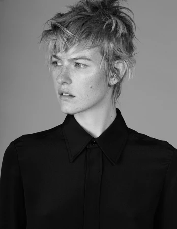 Black and white portrait of a woman with short tousled hair wearing a dark collared shirt against a grey background.