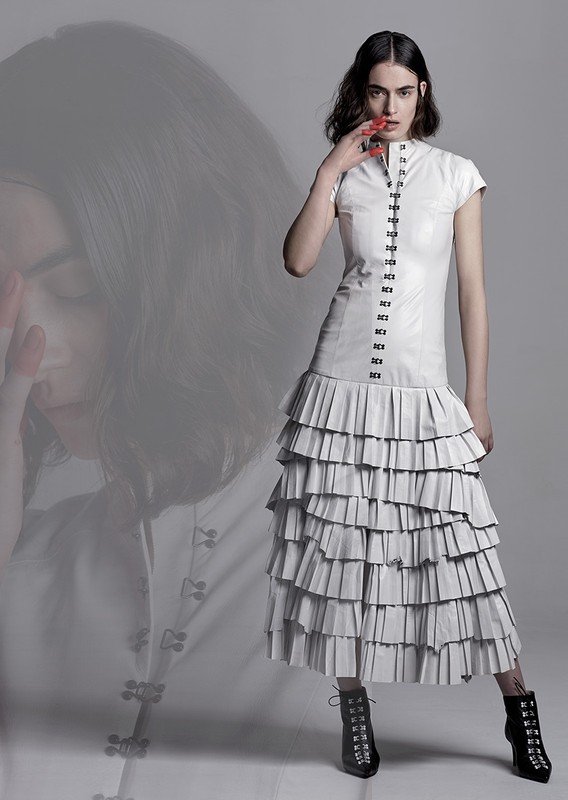 Model in white dress with tiered pleated skirt and black lace-up boots against a grey background