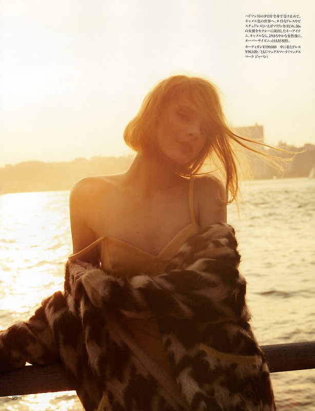 Woman in a strappy top and fur coat posing at the end of a pier on a sunny day. Los Angeles coastline is visible in background.