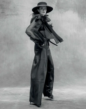 Model in wide trousers and sheer blouse wearing a wide-brim hat in a black and white editorial portrait