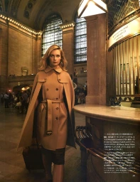 Woman in a beige double-breasted belted coat with caped shoulders standing inside Grand Central Terminal with arched windows