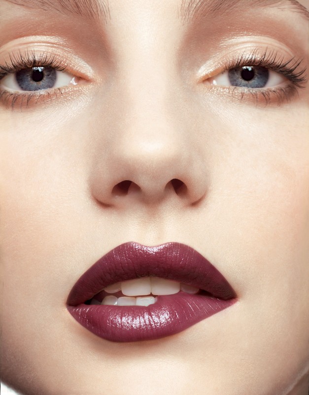 Close-up portrait of a fair-skinned adult female with light blue eyes and parted lips with dark purple lipstick, looking at the camera.