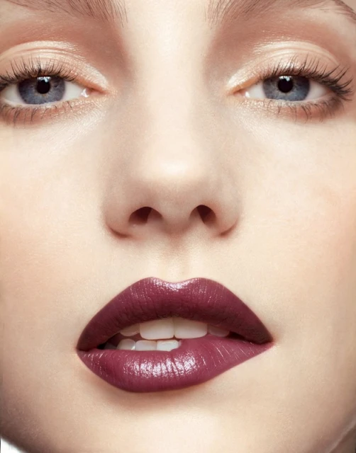 Close-up portrait of a fair-skinned adult female with light blue eyes and parted lips with dark purple lipstick, looking at the camera.