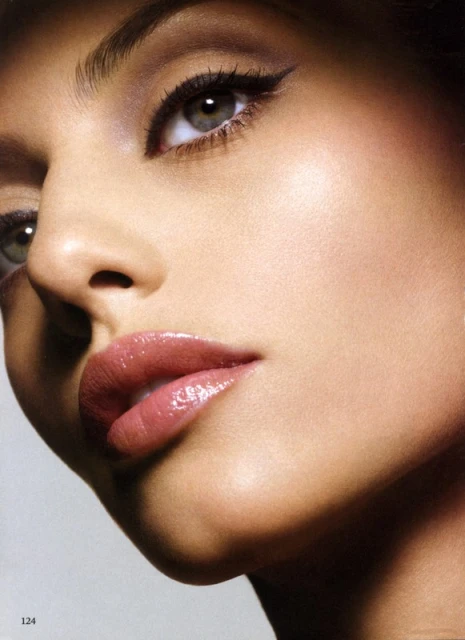 Close-up studio shot of a young adult woman with grey eyes and glossy lips wearing eyeliner. Beauty and cosmetics concept.