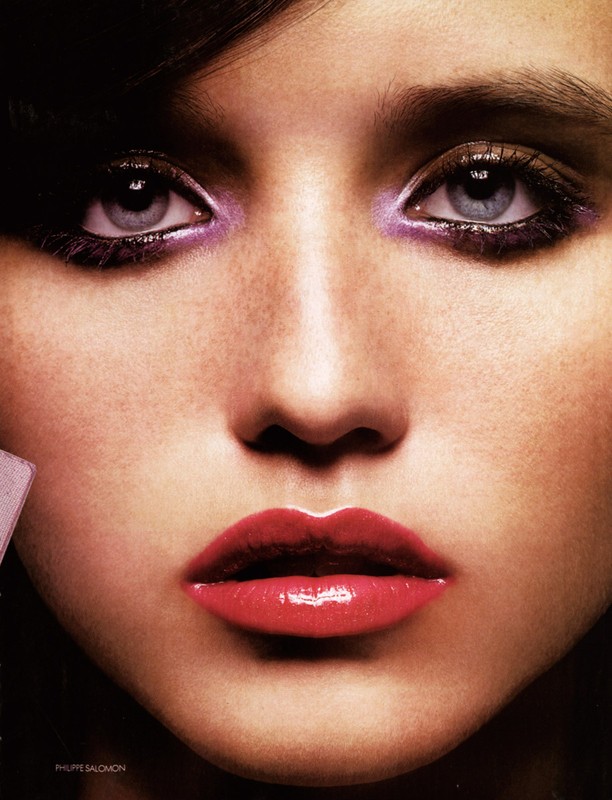 Close-up portrait of a woman with dramatic eye makeup and glossy red lips against a dark background, with a beauty and fashion aesthetic.