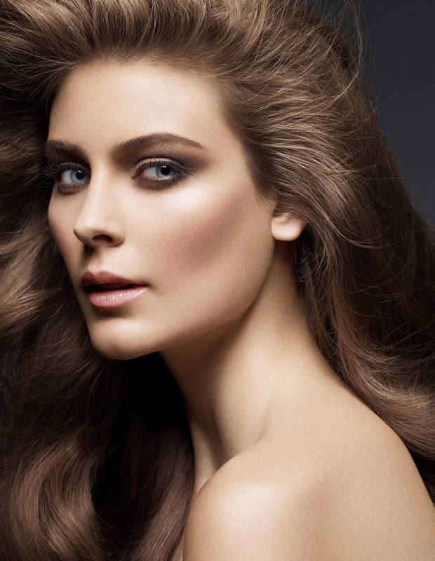 Close-up portrait of a fair-skinned adult female with long brown wavy hair, wearing smoky eye makeup, and posing in a studio.