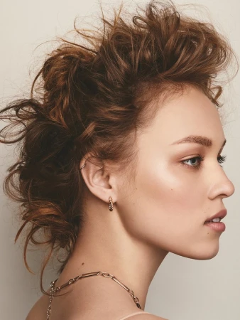 Profile portrait of a woman with tousled brown hair, hoop earrings, and neutral makeup against a plain light background
