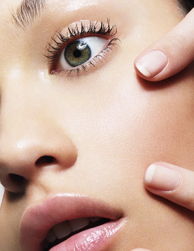 Close-up macro portrait of a woman showing detailed skin texture, green eye with dark mascara, and fingers touching her face.