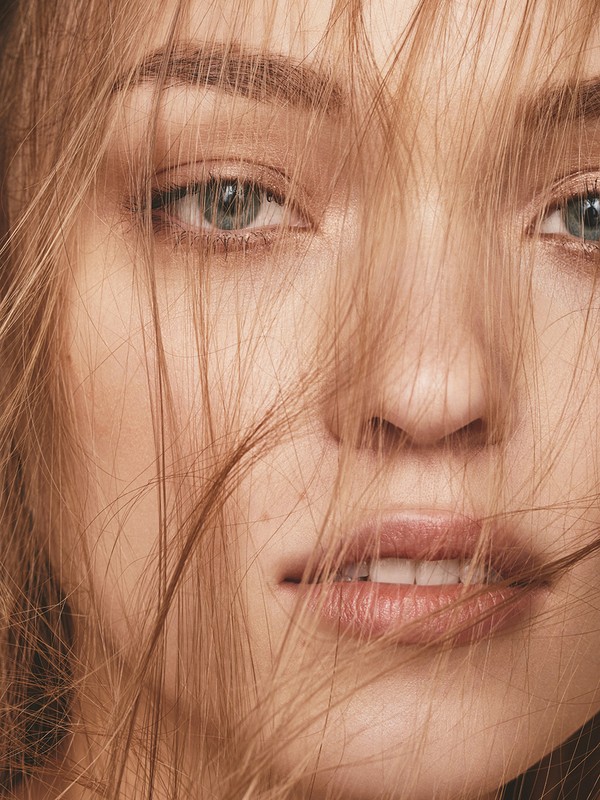 Close-up beauty portrait of a woman with loose blonde hair falling across her face and natural makeup by Keiko Takagi.