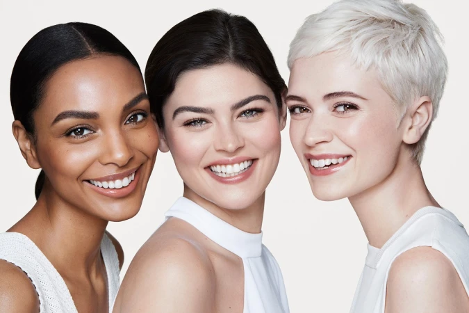 Close-up portrait of three smiling diverse female models with natural makeup against a plain white background