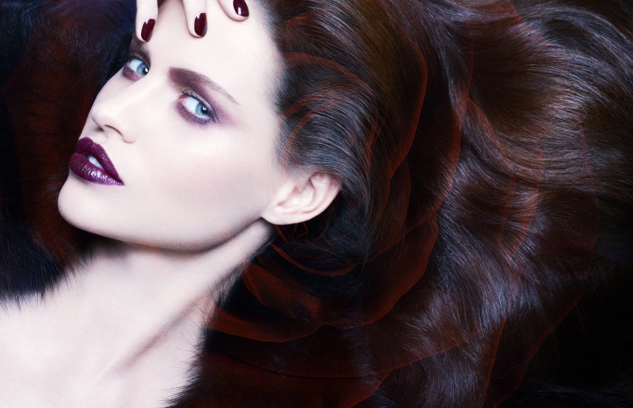 Close-up studio shot of a glamorous adult woman with dark burgundy hair, glossy purple lipstick, and stylish eyeshadow posing gracefully.