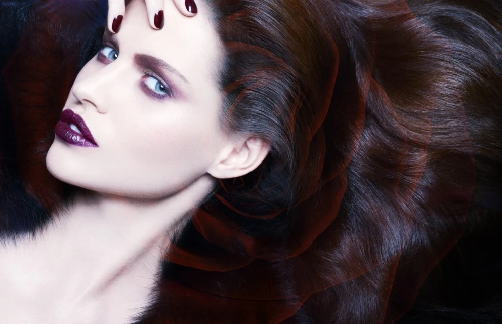 Close-up studio shot of a glamorous adult woman with dark burgundy hair, glossy purple lipstick, and stylish eyeshadow posing gracefully.