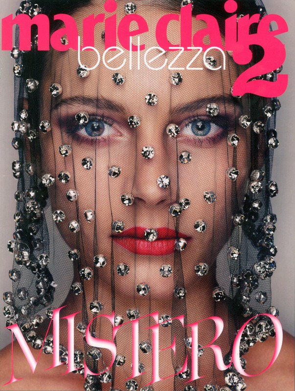 Close-up of a woman's face covered with a sheer, beaded veil. The magazine cover features 'Marie Claire' and 'Mistero' in pink font.
