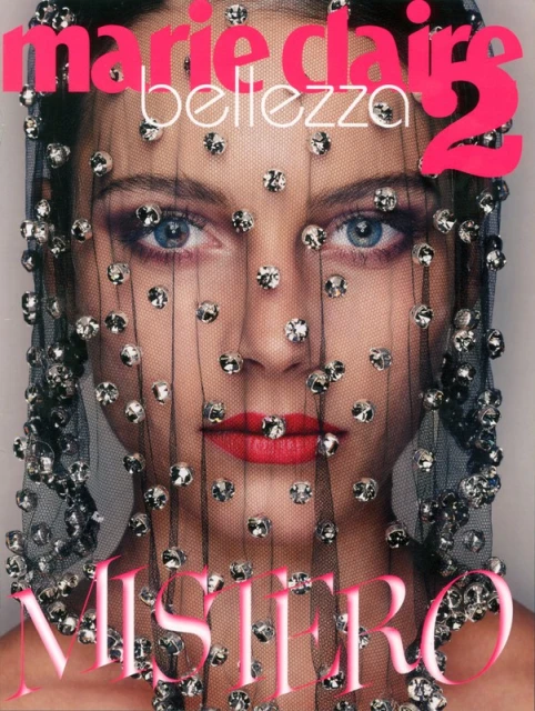 Close-up of a woman's face covered with a sheer, beaded veil. The magazine cover features 'Marie Claire' and 'Mistero' in pink font.
