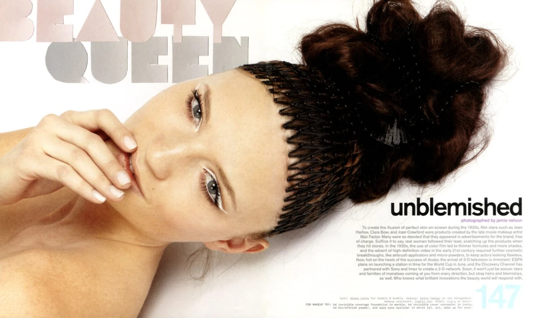Beauty portrait of a young woman with dark hair styled up, posing with hand near her lips, in a beauty editorial with magazine text visible.