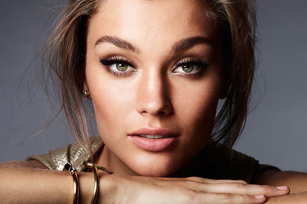 Close-up portrait of a woman with green eyes and gold bracelets against a gray backdrop, with focus on beauty and fashion.